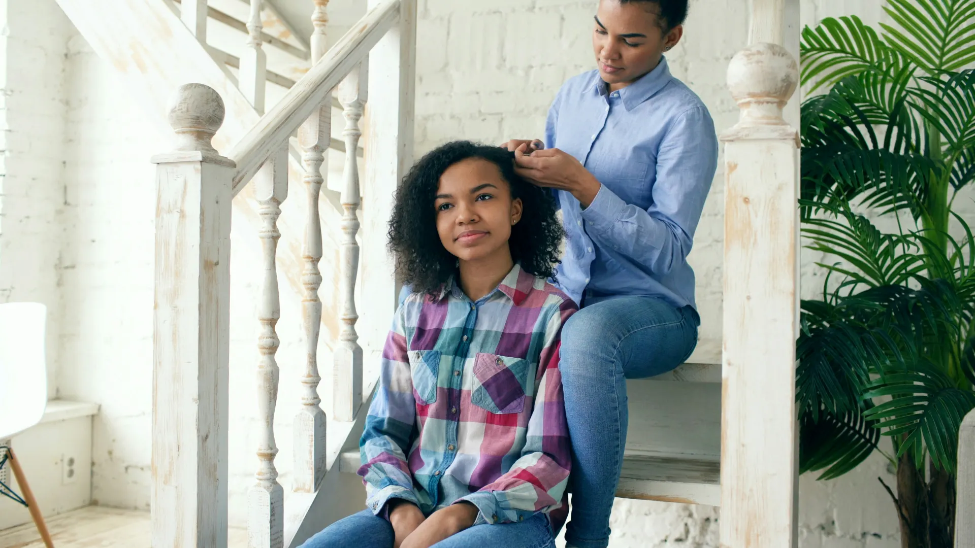 A mother braiding her daughter’s hair on a staircase